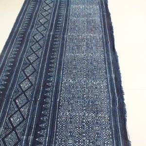 May include: A long piece of indigo blue fabric with a white geometric pattern. The fabric has a frayed edge and is folded in half.