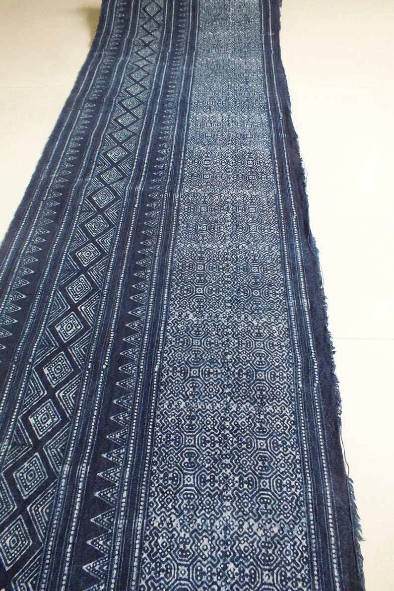 May include: A long piece of indigo blue fabric with a white geometric pattern. The fabric has a frayed edge and is folded in half.