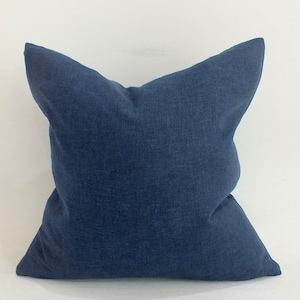 Puede incluir: Una almohada cuadrada de color azul oscuro con una tela de lino suave y texturizada.