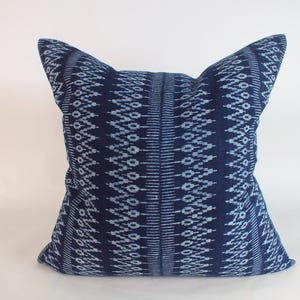 May include: A square throw pillow featuring a deep navy blue fabric with a repeating light blue geometric pattern. The design consists of vertical bands of intricate diamond and zigzag motifs that run across the entire surface of the cushion.