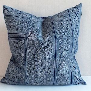 May include: A square throw pillow featuring a deep blue and white batik-style fabric with intricate geometric patterns, including repeating squares, diamonds, and linear stripes, finished with a visible side zipper closure.