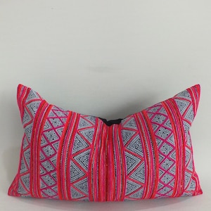 May include: A pink and blue patterned pillow with a geometric design. The pillow is made of a soft, woven fabric and has a black zipper closure.