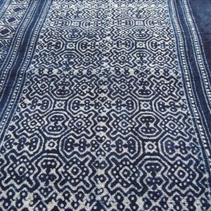 May include: A close-up of a blue and white fabric with a repeating geometric pattern. The fabric has a textured surface and a slightly faded appearance.