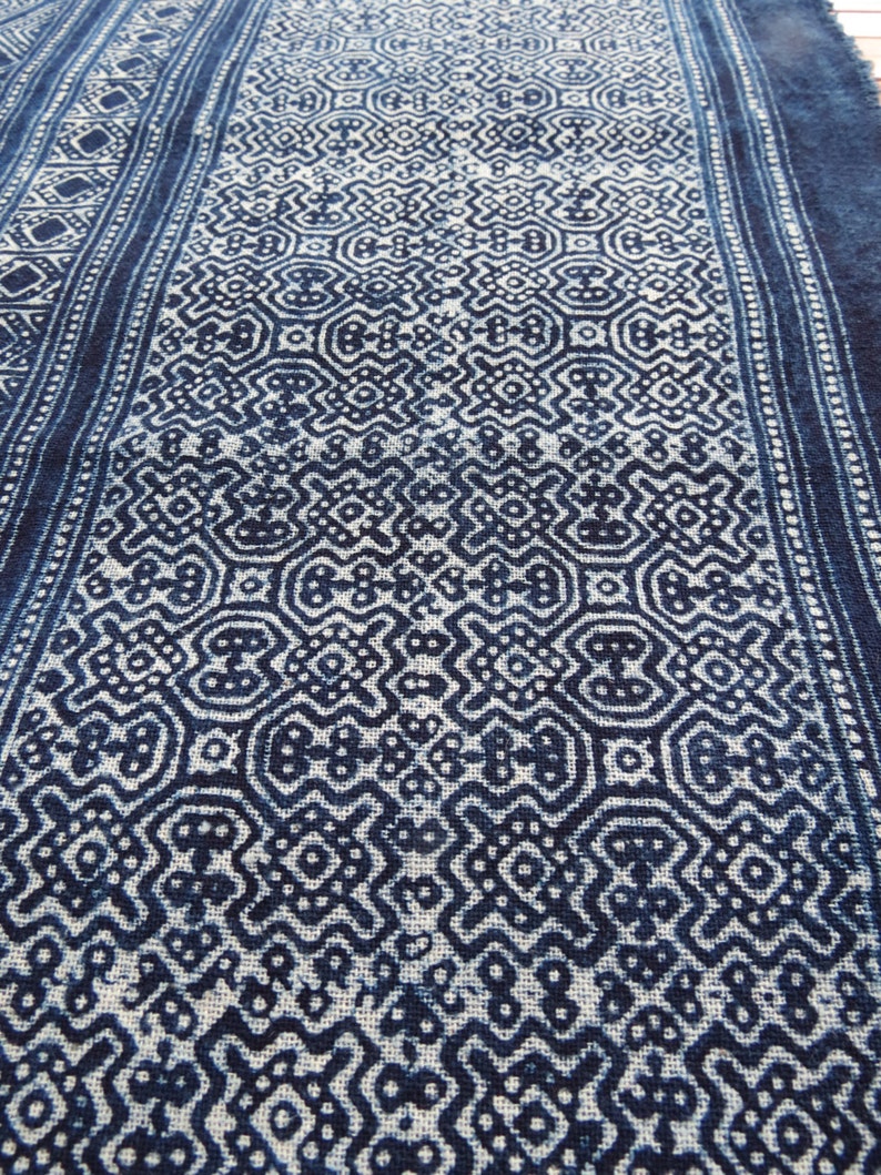 May include: A close-up of a blue and white fabric with a repeating geometric pattern. The fabric has a textured surface and a slightly faded appearance.