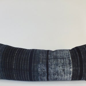May include: A long, rectangular pillow with a dark blue and white striped pattern. The pillow is made of a soft, textured fabric and has a subtle sheen.
