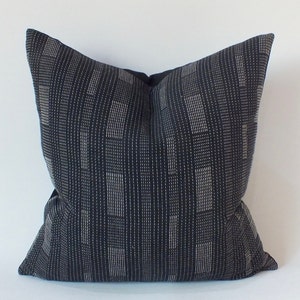 Puede incluir: Una almohada de tiro de patrón negro y blanco con un diseño geométrico. La almohada está hecha de una tela suave y texturizada.