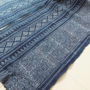 May include: A close-up of a blue fabric with a white geometric pattern. The fabric is folded in half and has a frayed edge.