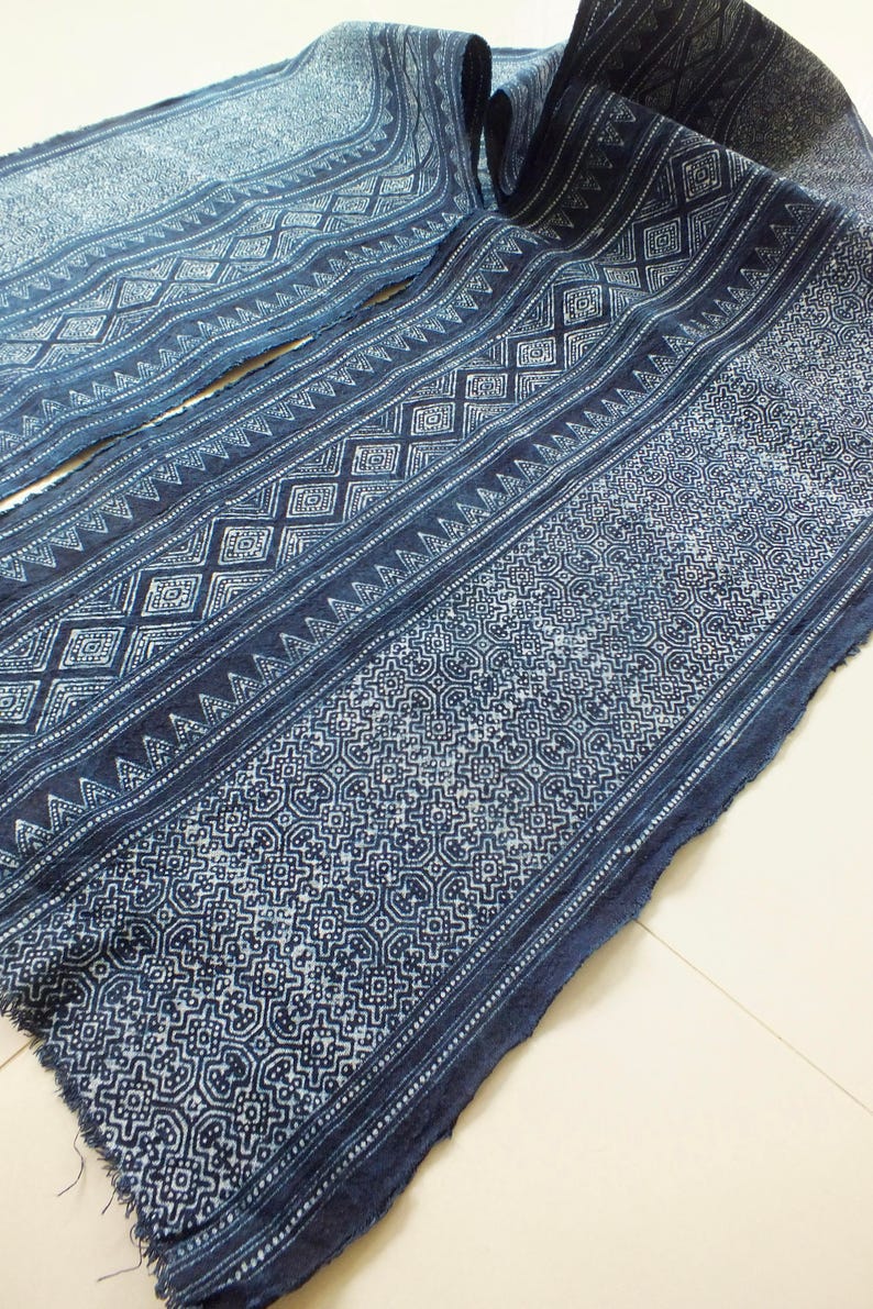 May include: A close-up of a blue fabric with a white geometric pattern. The fabric is folded in half and has a frayed edge.