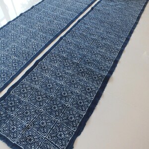 May include: A long, indigo blue fabric with a white geometric pattern. The fabric is folded in half and has a raw edge.