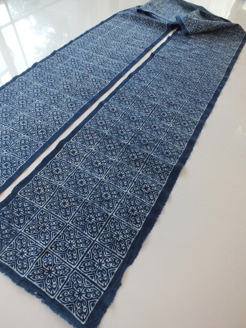 May include: A long, indigo blue fabric with a white geometric pattern. The fabric is folded in half and has a raw edge.