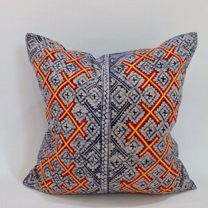 May include: A decorative pillow with a blue and white background and a geometric pattern of red and yellow crosses.
