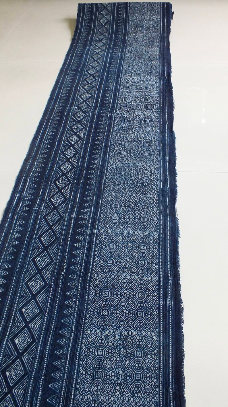 May include: A long piece of indigo blue fabric with a white geometric pattern. The fabric has a frayed edge and is folded in half.