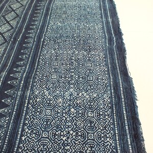 May include: A close-up of a blue and white indigo fabric with a geometric pattern. The fabric has a frayed edge and is woven with a fine texture.