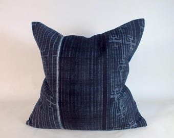 May include: A square throw pillow featuring a deep indigo blue fabric with a central panel of vertical pinstripes flanked by side sections displaying a geometric maze-like pattern in lighter shades of blue and white across the entire surface.