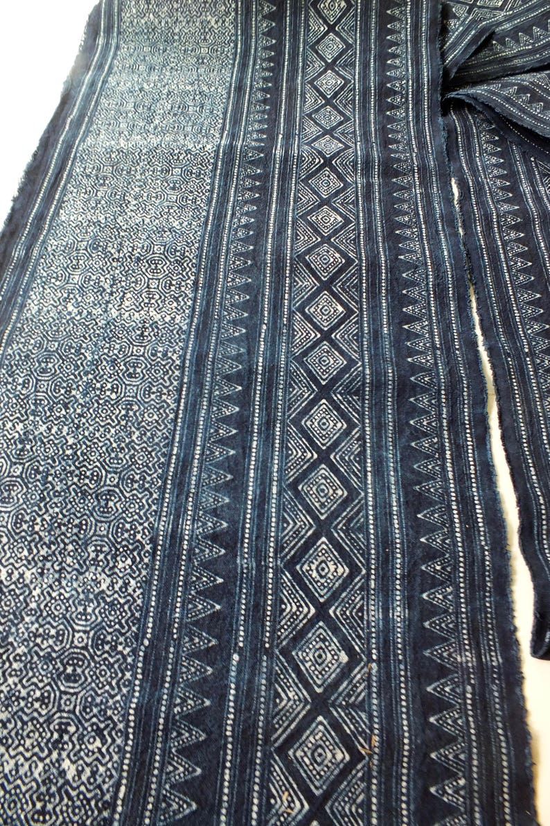 May include: A close-up of a blue and white fabric with a repeating geometric pattern. The fabric is woven and has a textured surface.