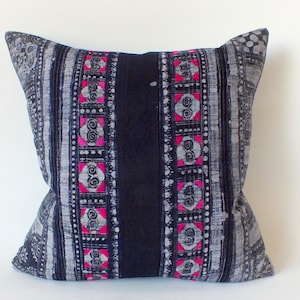 May include: A black and white patterned cushion with pink accents. The cushion has a geometric design with a central black stripe.