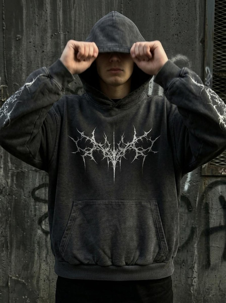 May include: Dark gray hoodie with a white, spiky graphic on the front and lightning bolt designs on the sleeves. The hoodie has a drawstring hood and a front pocket. The garment is made of a soft, textured material.