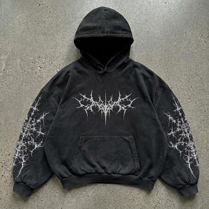 May include: Dark gray hoodie with a front pocket and a hood. The hoodie features a white, spiky graphic on the front and on the sleeves. The garment has a washed, vintage look.