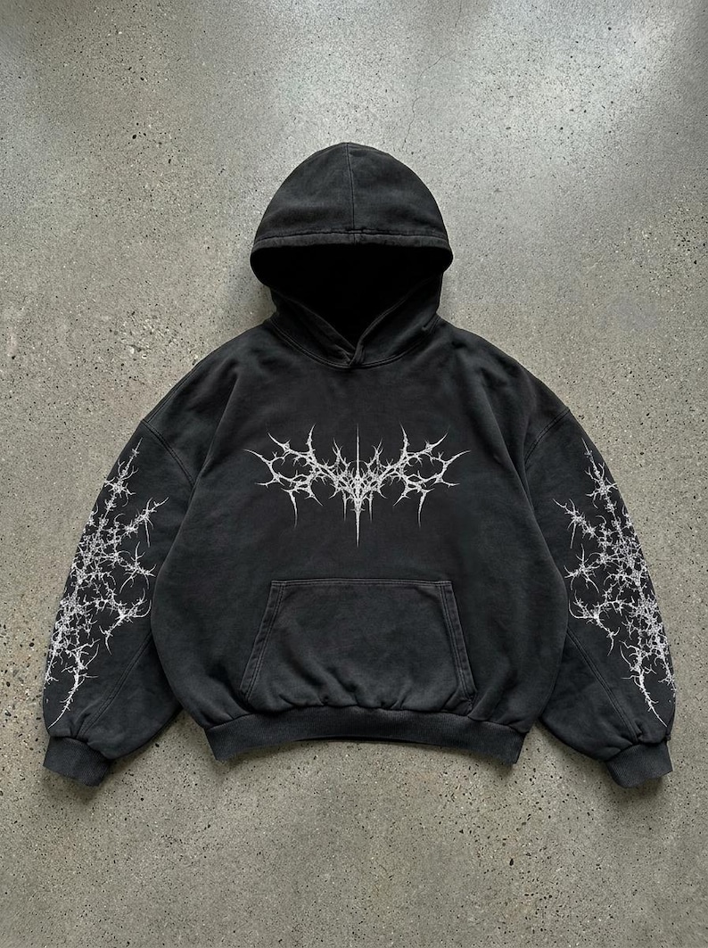May include: Dark gray hoodie with a front pocket and a hood. The hoodie features a white, spiky graphic on the front and on the sleeves. The garment has a washed, vintage look.