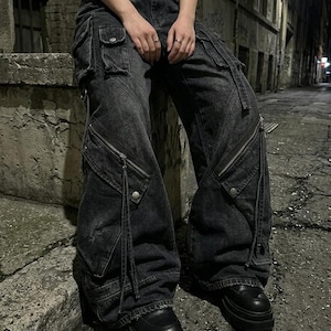 A person sitting on a concrete ledge at night wearing black utility cargo denim pants with prominent pockets and thick-soled shoes.