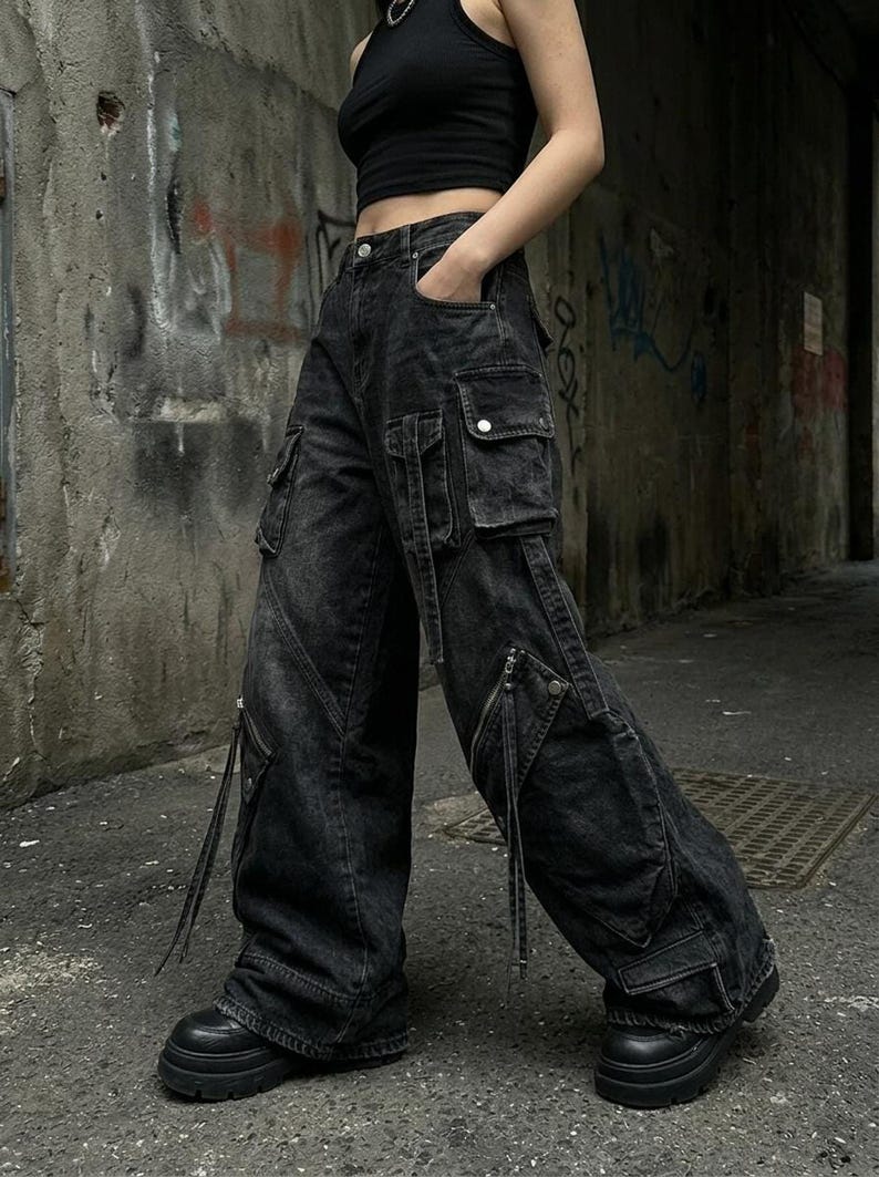 A side-angle view of a person wearing black distressed cargo jeans with prominent side pockets and straps in an urban alley.