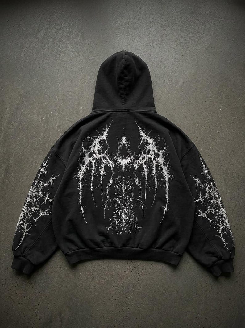 May include: Black hoodie with a white, intricate, spiky design on the back and sleeves. The design has a gothic or abstract aesthetic. The hoodie has a hood and ribbed cuffs and hem.
