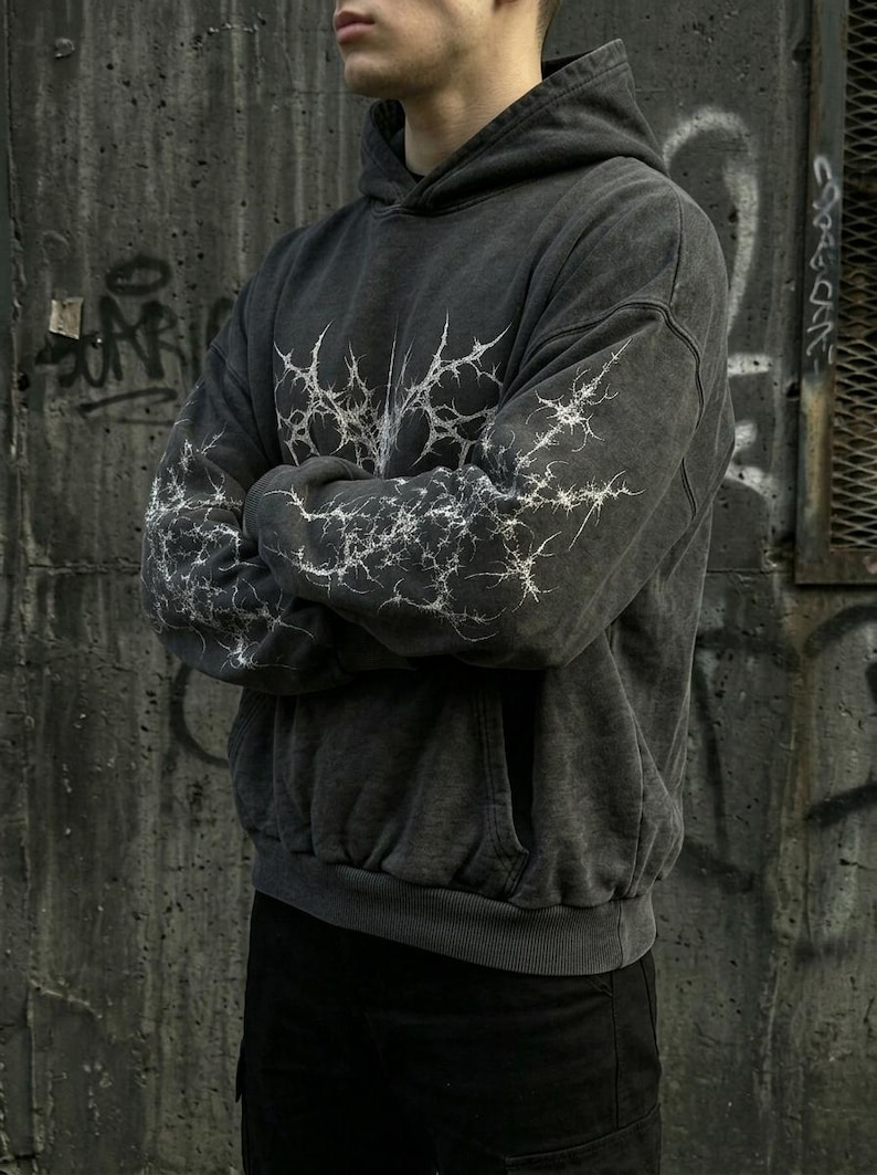 May include: Dark gray hoodie with a white lightning bolt design on the chest and sleeves. The hoodie has a front pocket and a drawstring hood. The garment is made of a soft, washed fabric.