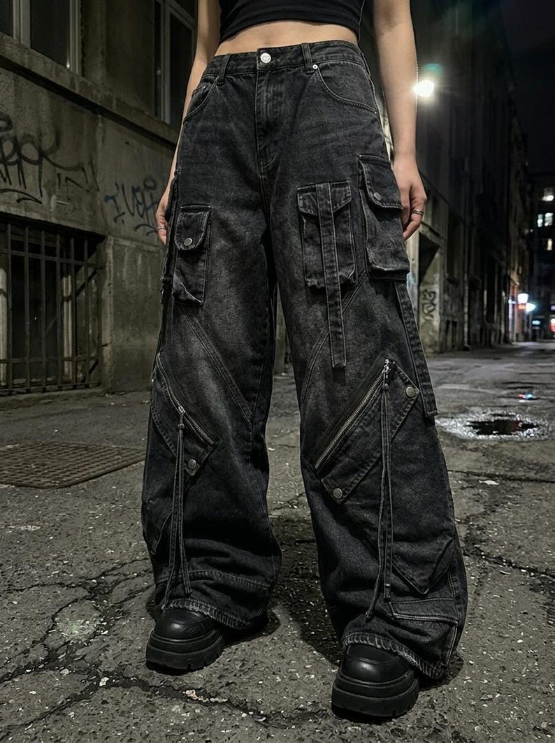 A close-up of the front of a person wearing black baggy cargo pants with diagonal zippered pockets, standing on a paved street at night.