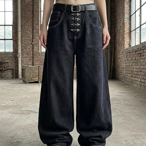 May include: Black wide-leg denim jeans featuring a high-waisted fit with a black leather belt. The front closure includes a vertical row of four silver-toned metal toggle clasps and white contrast stitching along the pockets and seams.