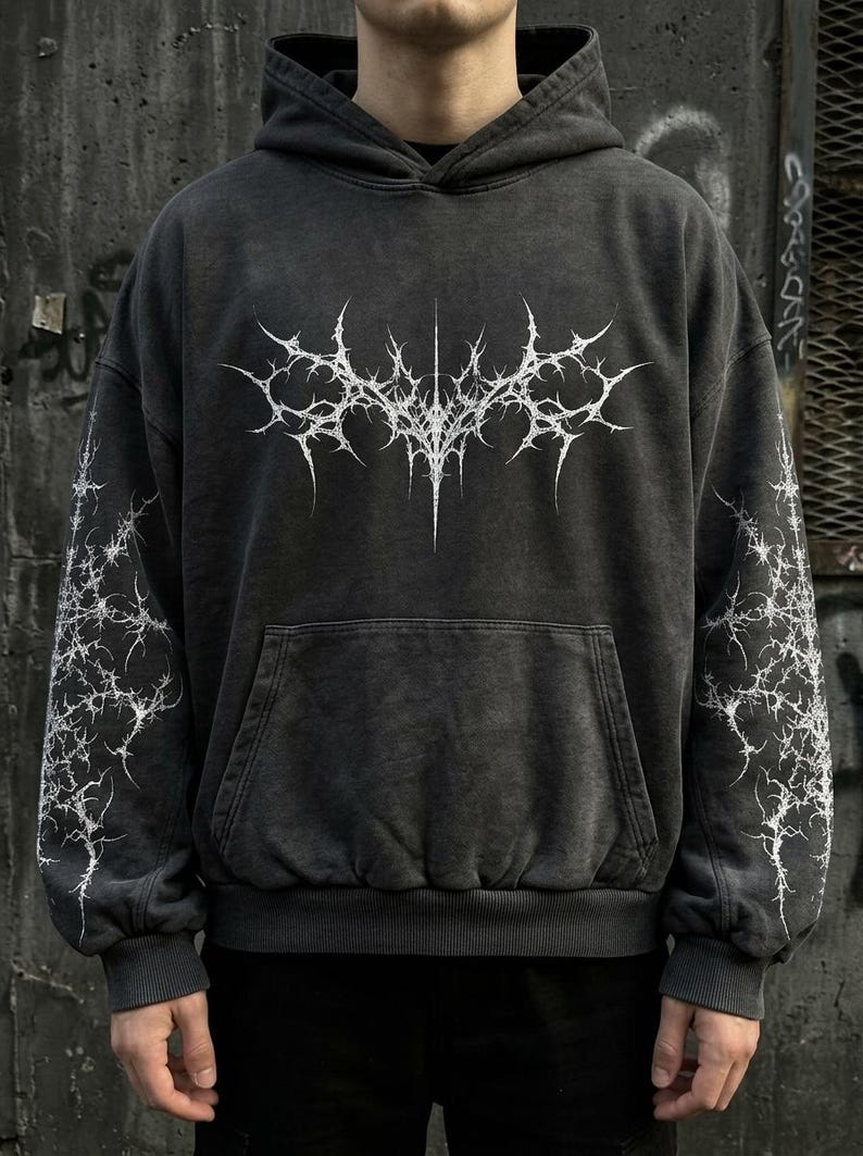 May include: Dark gray hoodie with a white, spiky graphic on the front and sleeves. The hoodie has a kangaroo pocket and a drawstring hood. The fabric has a washed, vintage look. The design is a gothic or edgy style.