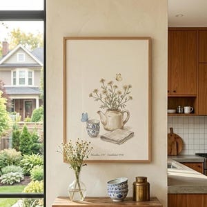 以下が含まれることがあります： ティーポット、ティーカップ、花、蝶を描いた水彩画の額入りプリント。木製のキャビネットの上に飾られており、装飾的なボウルと花瓶が置かれています。「Hamilton, ON - Established 1946」の文字が見えます。