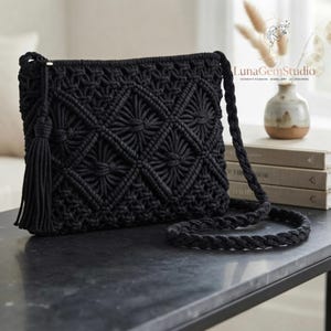 May include: A black macrame crossbody bag featuring a detailed diamond knot pattern across the front, a long braided shoulder strap, and a decorative tassel attached to the side. The bag is constructed from thick cord with a textured finish.