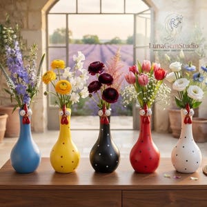 Può includere: Cinque vasi in ceramica a forma di gallina, ognuno con collo lungo, bargigli rossi e becco. I vasi sono blu, gialli, neri a pois bianchi, rossi a pois neri e bianchi a pois neri, ognuno contenente un bouquet di fiori freschi.