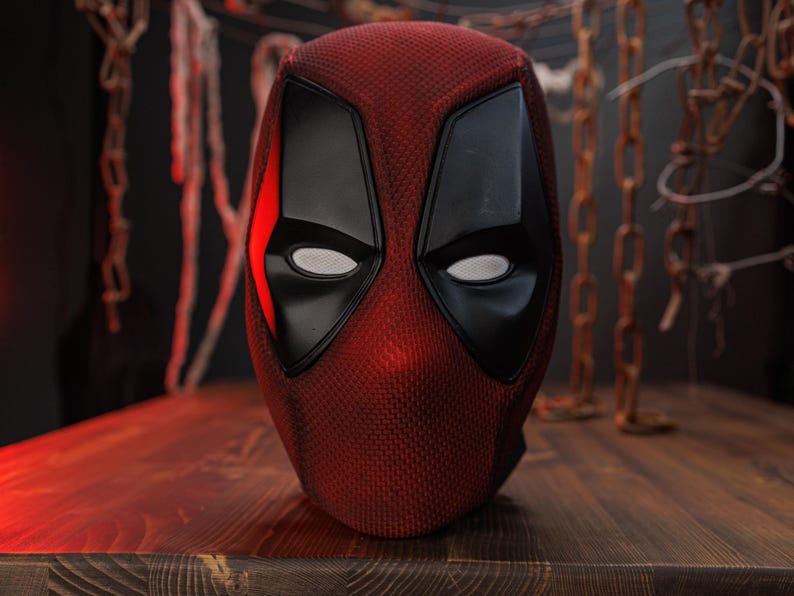 K&ouml;nnte beinhalten: Eine rot-schwarze Vollkopfmaske mit einer strukturierten Stoffoberfl&auml;che, glatten schwarzen Augenpartien mit wei&szlig;en Netzgl&auml;sern und einem markanten kantigen Design. Die Maske zeigt eine leuchtend rote Farbe auf dem Hauptteil mit schwarzen Akzenten.