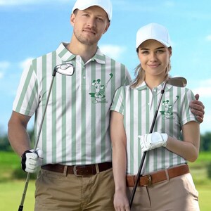 May include: Matching green and white striped golf shirts with a cartoon graphic and the name "Smiths". The shirts have a collared neckline and are paired with khaki pants and a brown belt. Both individuals are wearing white golf hats.