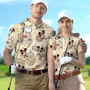 May include: Two people wearing matching beige polo shirts with a pirate-themed Mickey Mouse print. The shirts feature a repeating pattern of Mickey Mouse, ships, and compasses. Both are wearing white caps and holding golf clubs.