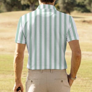 May include: A short-sleeved polo shirt with vertical stripes in white and light green. The shirt is paired with khaki-colored pants. The image is taken from the back, showing the shirt's pattern and the overall casual style.