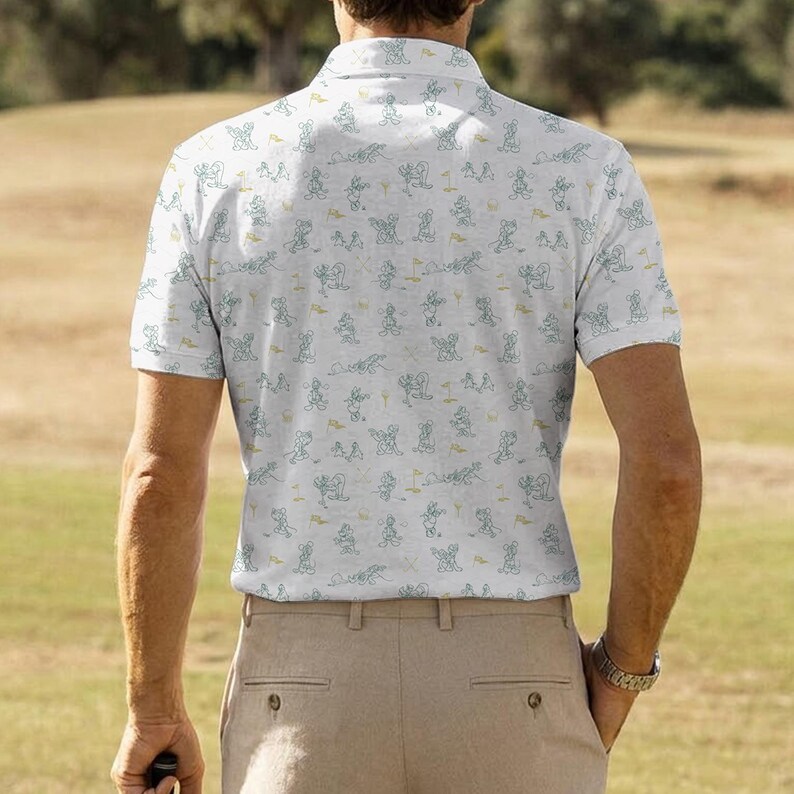 Może przedstawiać: Biała koszulka polo z golfowym wzorem w kolorze jasnoniebieskim i ż&oacute;łtym. Koszula ma kr&oacute;tkie rękawy i kołnierzyk zapinany na guziki. Osoba ma na sobie spodnie khaki i srebrny zegarek.