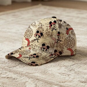 May include: A beige baseball cap featuring a pirate map design with cartoon Mickey Mouse characters wearing bandanas and eye patches. The cap has a curved brim and a black button on top.