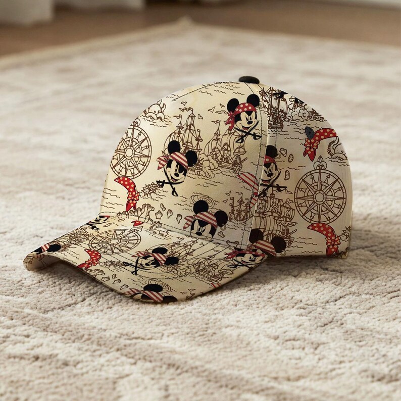 May include: A beige baseball cap featuring a pirate map design with cartoon Mickey Mouse characters wearing bandanas and eye patches. The cap has a curved brim and a black button on top.