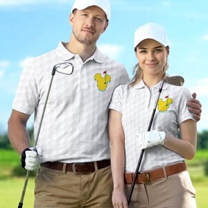 May include: Two people wearing white golf polo shirts with a golf ball pattern and a yellow Mickey Mouse-shaped logo. They are wearing white caps and khaki pants, holding golf clubs. The background is a blue sky and green grass.