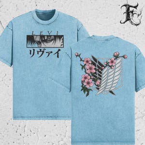 May include: A light blue acid-wash t-shirt featuring a graphic of Levi's eyes with the text LEVI and Japanese characters on the front. The back displays a white wing emblem intertwined with pink cherry blossoms and green leaves.