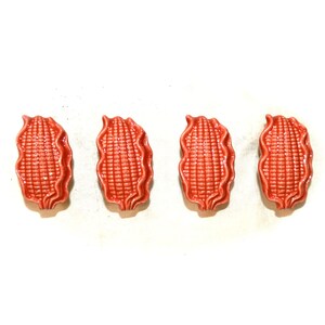 May include: Four ceramic corn on the cob drawer pulls in a reddish-orange color.