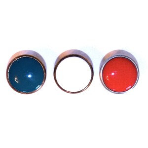 May include: Three small, round objects with a metallic rim. One is teal, one is white, and one is red. The objects are arranged in a row against a white background. These could be decorative buttons or small jewelry pieces.