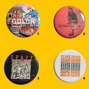 May include: Four round pinback buttons with unique designs. One button features the word "GULCH" with an illustration. Another has "ULTRA-VIOLENT" text and a graphic. A third button says "SPAZZ" with a band illustration. The last button says "EARTH CRISIS".