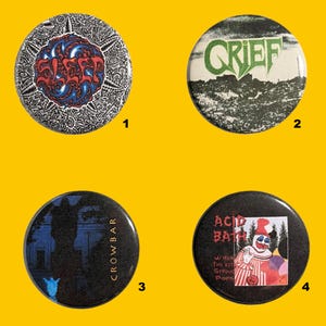 May include: Four round pinback buttons with various designs. One features the word "SLEEP" in red and blue on a black and white patterned background. Another has the word "GRIEF" in green. A third has "CROWBAR" and a silhouette. The last has "ACID BATH".