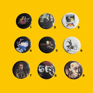 Puede incluir: Nueve insignias redondas con varios diseños. Las insignias presentan imágenes de carteles de películas, fotos de bandas y arte gráfico. Las insignias son negras, blancas y de varios colores, con texto e imágenes. Las insignias están dispuestas sobre un fondo amarillo.