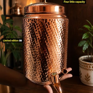 Op de afbeelding: Een cilindrische koperen waterdispenser met een gehamerde textuur, een bijpassend deksel met een kleine knop en een functionele kraan aan de onderkant. De tekst "Limited edition" en "Four little capacity" is zichtbaar op de afbeelding.
