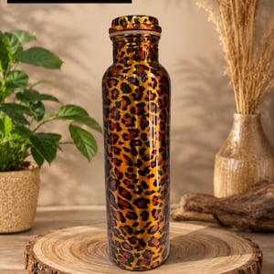 Può includere: Una borraccia cilindrica in metallo con un motivo leopardato lucido nei toni del marrone, nero e oro. La bottiglia ha un tappo a vite abbinato e riporta il testo "Leopard bottle" e "Two piece available buy now fast".