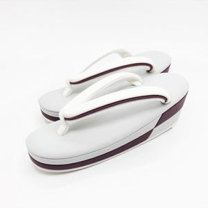 May include: A pair of zori sandals featuring light gray footbeds and thick white thong straps with dark maroon piping. The platform soles are layered with a matching dark maroon accent band along the side, providing a clean and structured appearance.